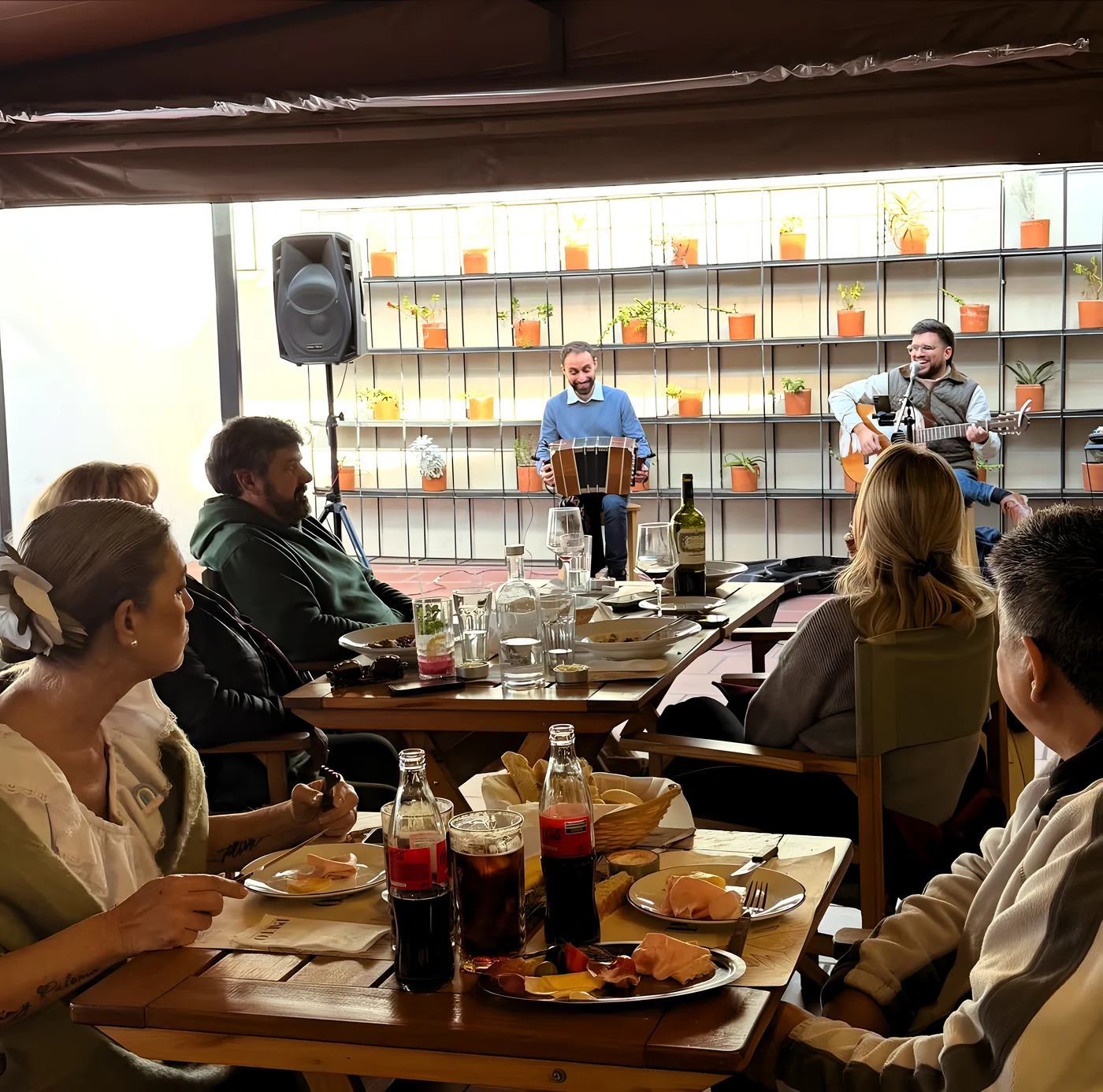 Terraza de Palto con las mesas ocupadas, gente comiendo bajo la pared de macetas